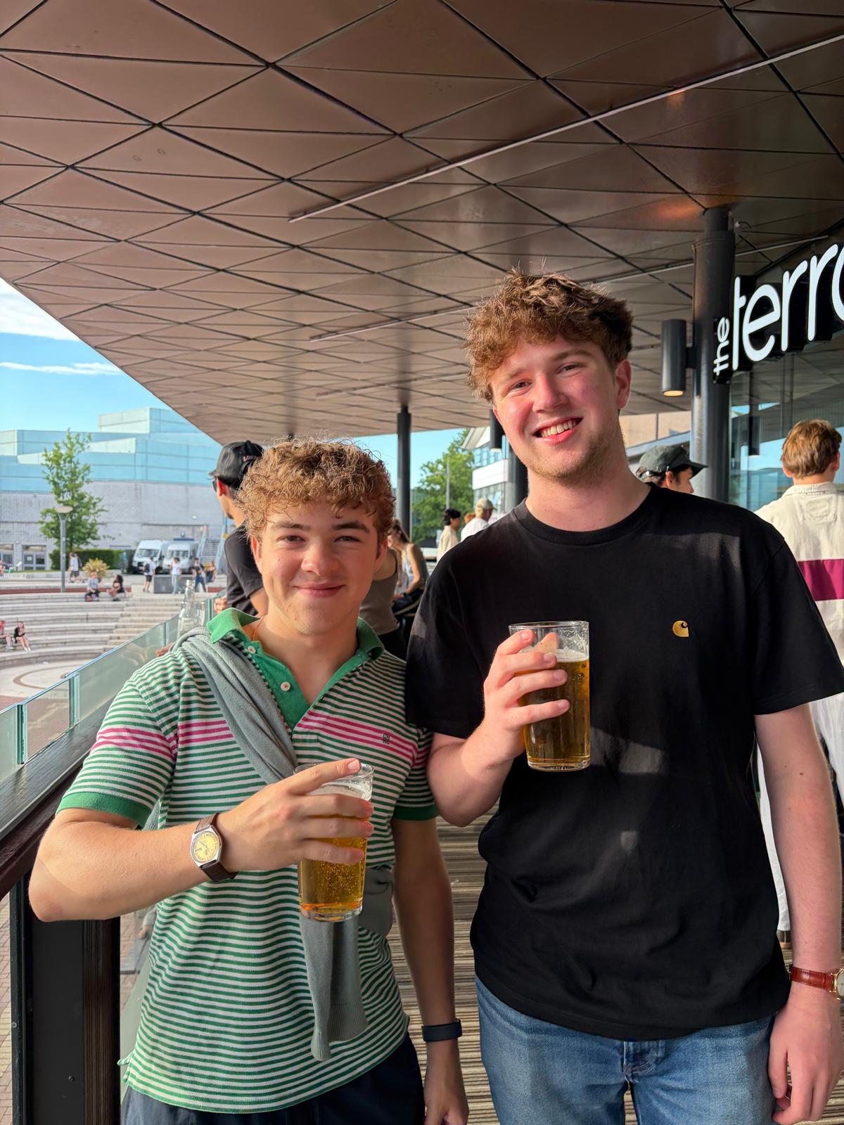 Two members holding pints on a sunny terrace